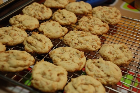 Eighteen freshly-baked toffee bit cookies cooling on a wire rack.